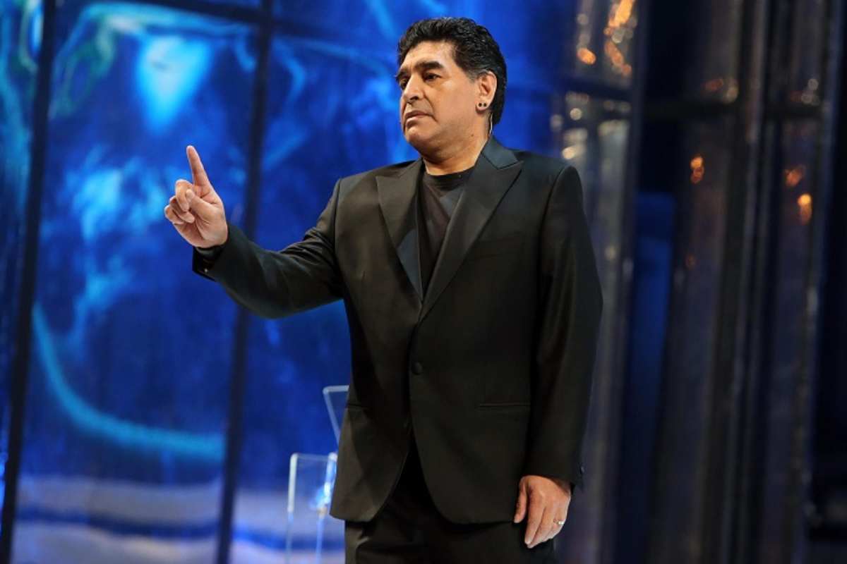 Diego Armando Maradona in abito elegante con il dito alzato su sfondo blu